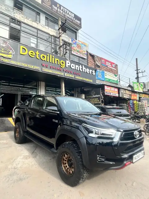 The studio's branded storefront on Shiv Mandir Chowk, with a black lifted Toyota Hilux pickup parked outside and the shop's own signboard listing paint protection film, ceramic coating, car wrap and interior customisation.
