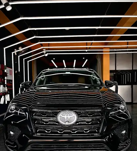 A black SUV's front grille and bonnet reflecting the studio's arched ceiling lights, photographed head-on inside the bay.