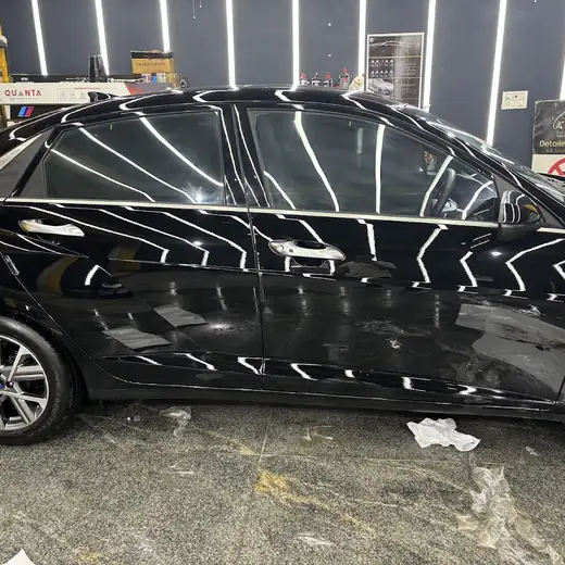 A black sedan's rear door and flank inside the studio, with paint protection film masking lines visible in the reflection and the studio's own Detailing Panthers sign on the wall behind it.