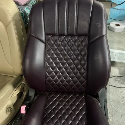 A close-up of a dark maroon diamond-stitched car seat inside the workshop, with foam and other seat covers stacked beside it.