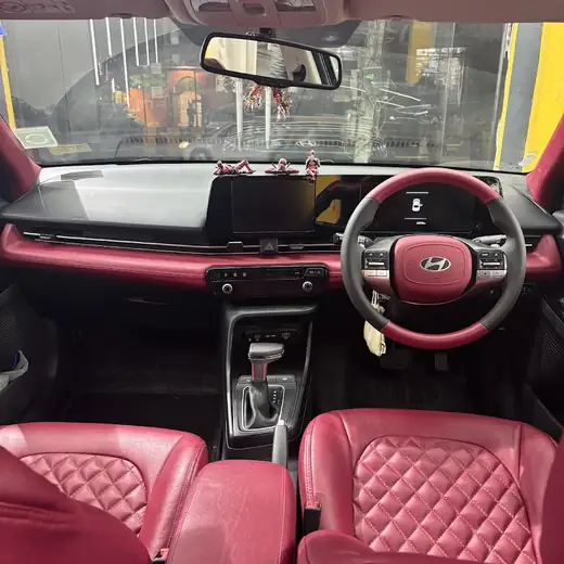The dashboard and front seats of a car finished in red leather with diamond stitching, seen from the rear seat looking toward the steering wheel.